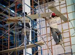 Two construction workers balancing precariously on scaffolding frames without guardrails or harness