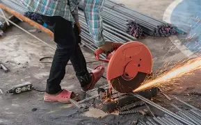 Worker cutting steel rebar with chop saw wearing pink rubber sandals