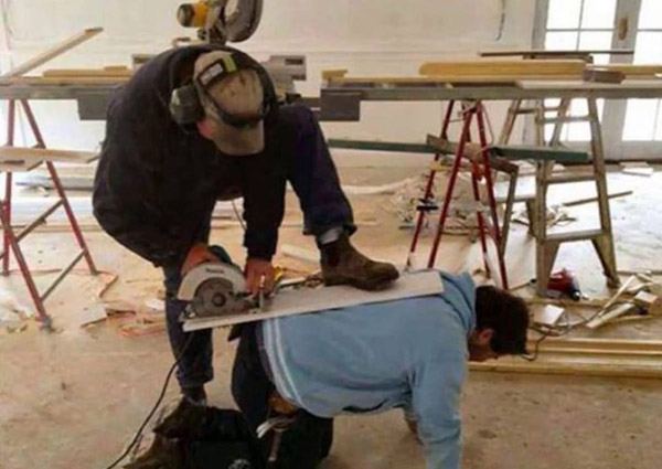 Worker using circular saw on top of coworker's back